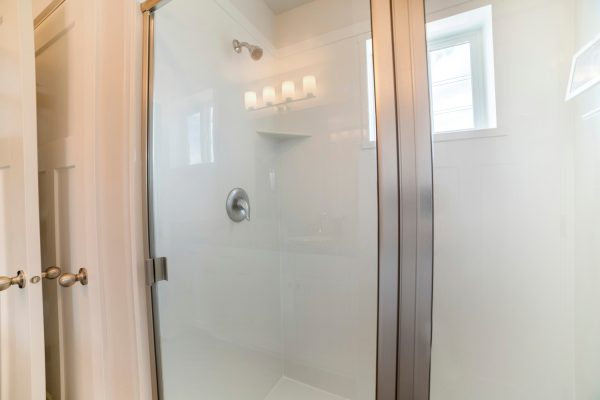 Bathroom interior of a shower stall with glass and stainless steel. There is a white door, wall mounted shower head inside and a window - Can You Paint A Fiberglass Shower [And How To]
