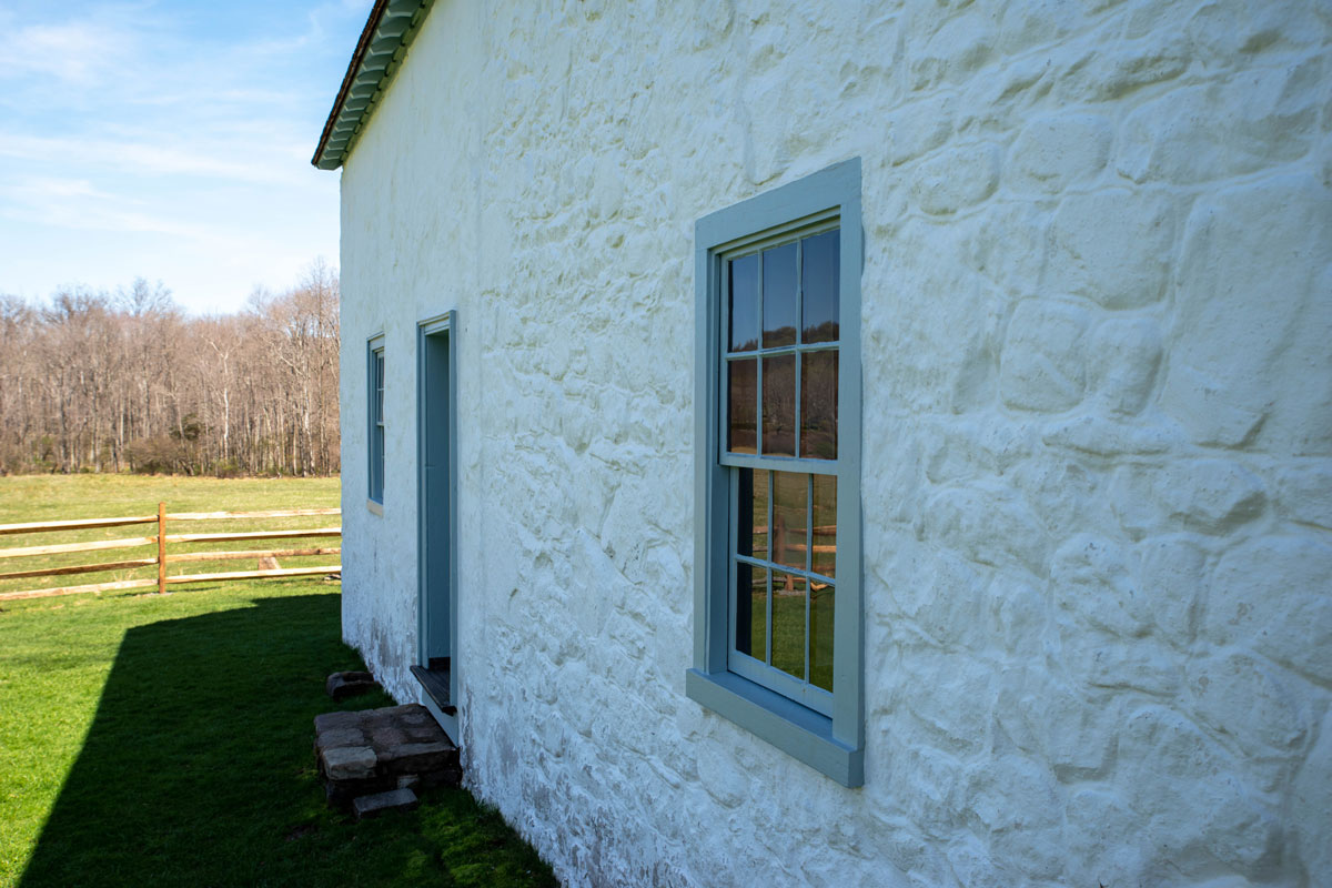 Beautiful sude view of a whitewashed stone cottage with blue window rim and antique window panes with rural scene reflection