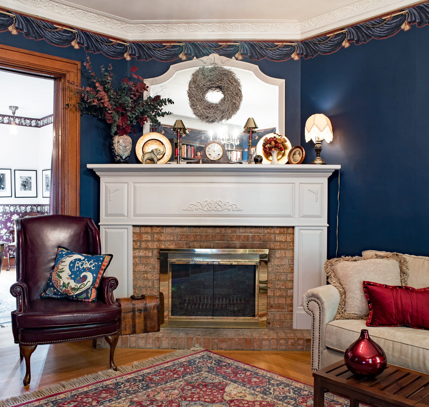 Brick fireplace with painted mantel in a Victorian living room with navy blue walls & ten foot ceiling in one hundred-year-old home.