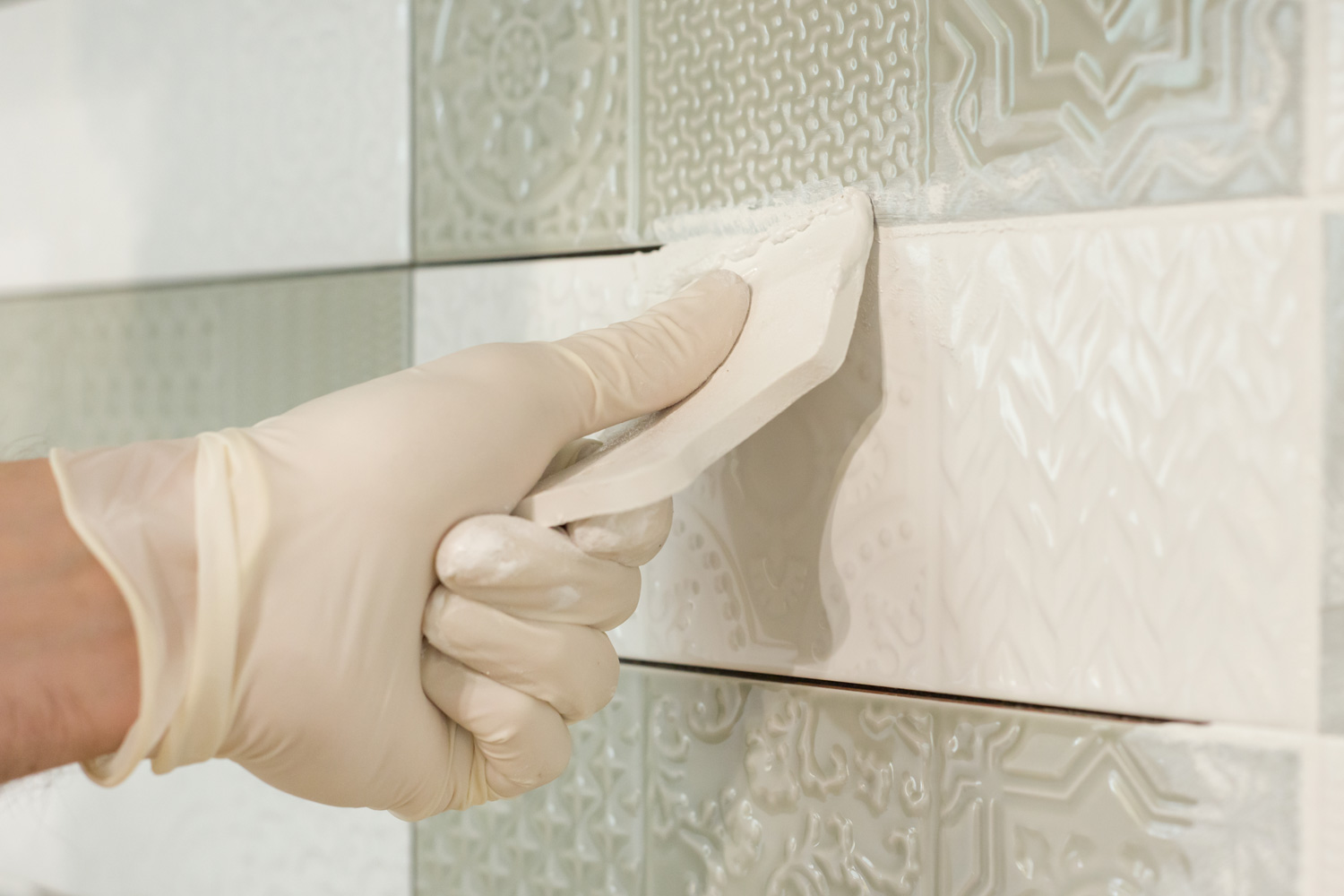 Closeup of tiler hand rubbing tile, Installing and grouting decorative finishes in environments with an high aesthetic value. Two-component, decorative, acid resistant epoxy grout.