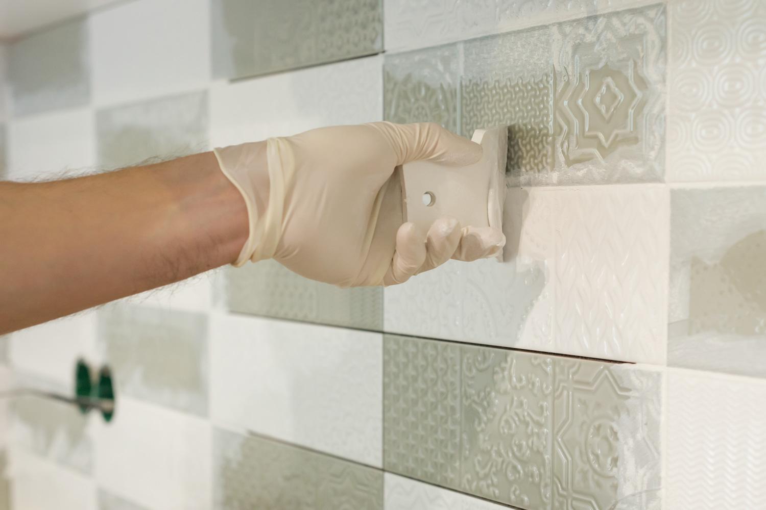 Closeup of tiler hand rubbing tile, Installing and grouting decorative finishes in environments with an high aesthetic value. Two-component, decorative, acid resistant epoxy grout.