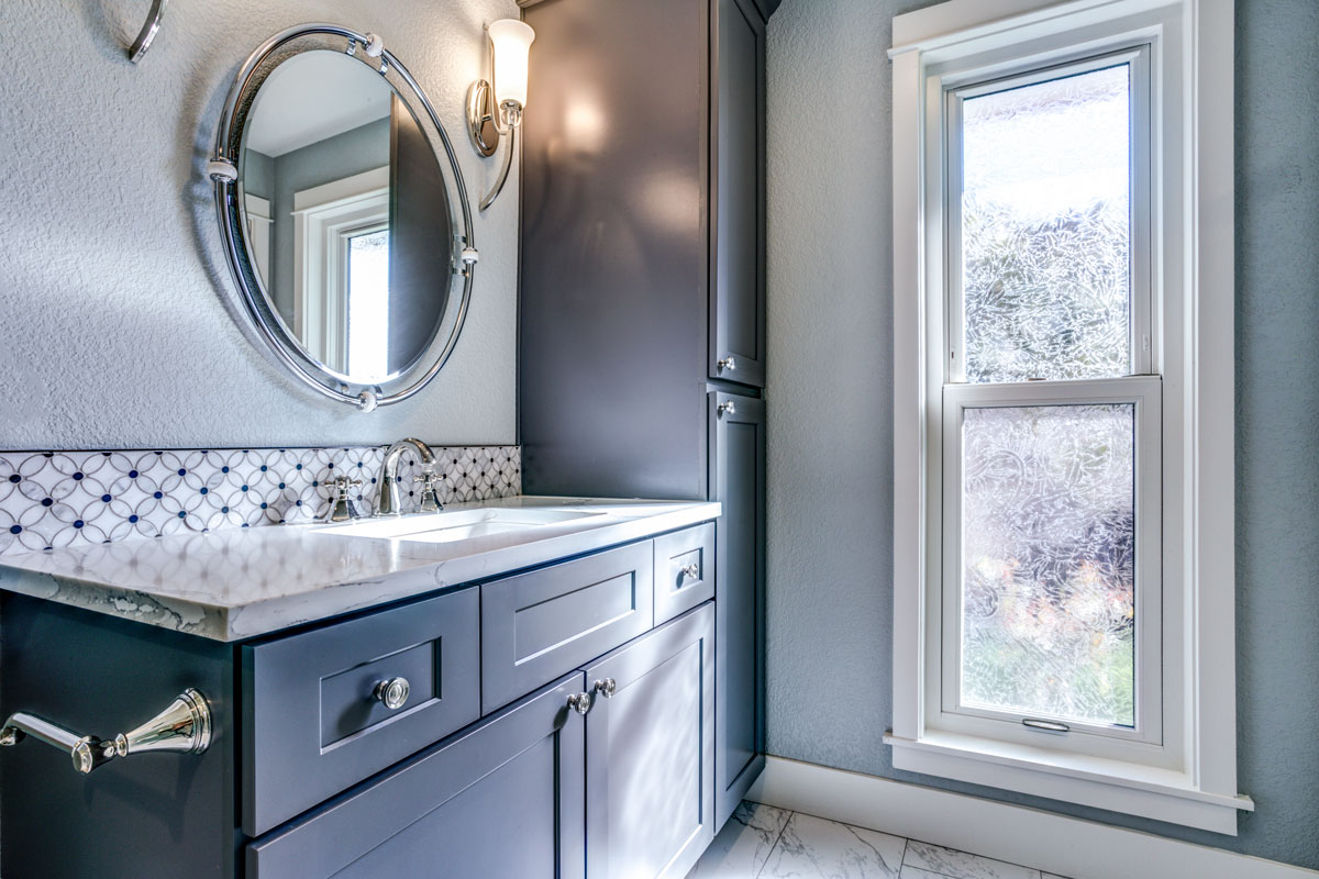 Classic inspired bathroom with gray painted cabinets matching a round mirror with wall lamps