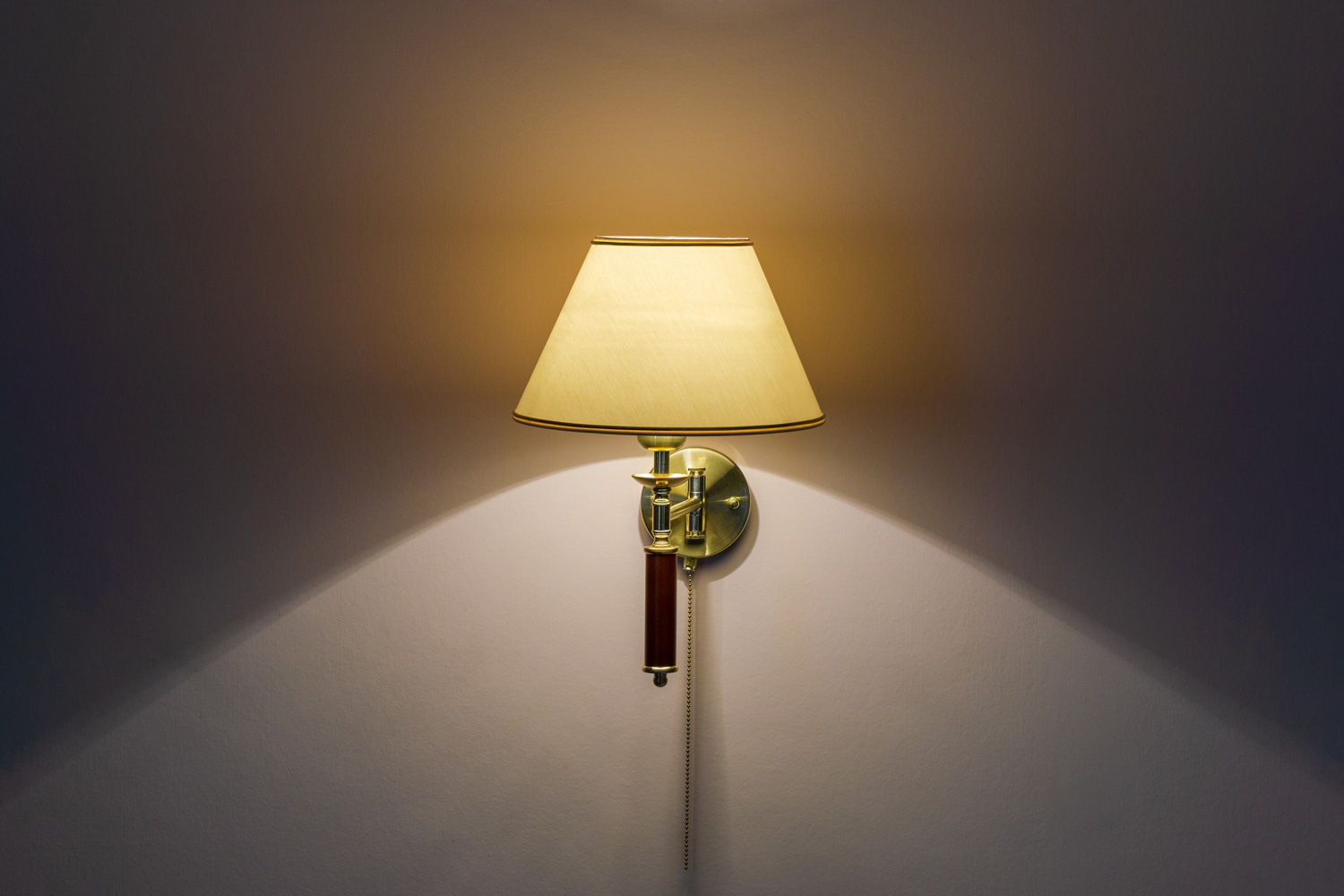 Classic sconce with turned on bulb under lampshade hanging on wall with beige wallpaper.