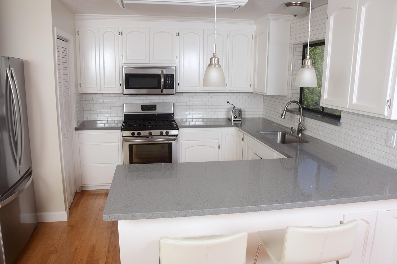 Classic small but open white domestic kitchen with subway tiles, stainless steel appliances and gray quartz counter tops