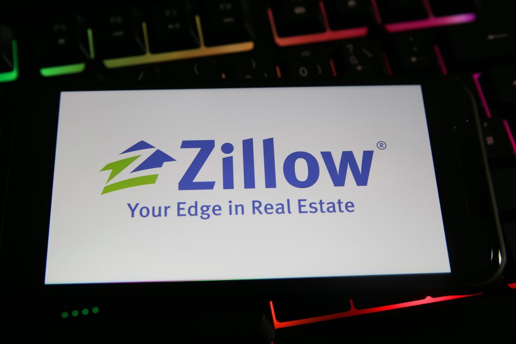 Closeup of mobile phone with logo lettering of zillow on computer keyboard