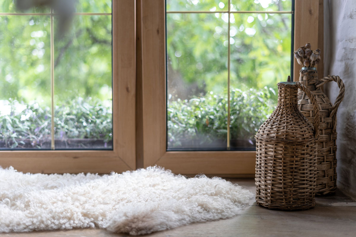 Comfort and cozy house with white and fluffy sheepskin rug, woven elements on bottle, dry plants on wooden windowsill in moder