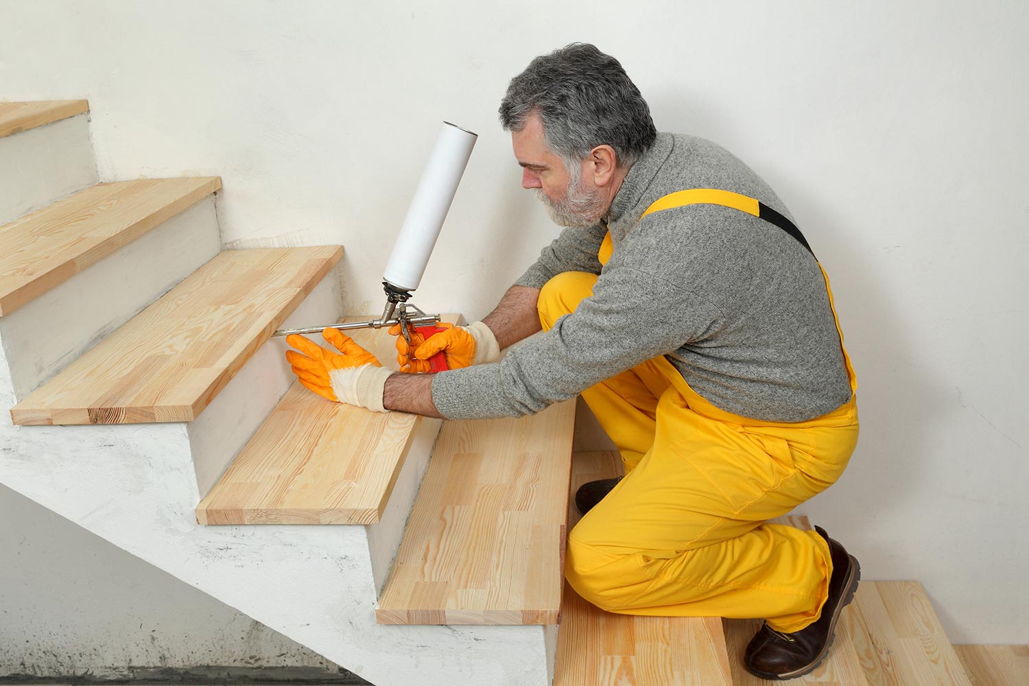 Construction worker fixing wooden stairs with polyurethane spray gun