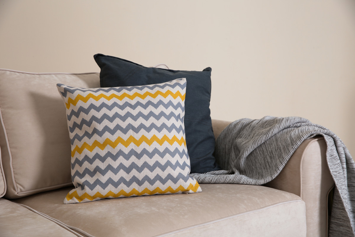 Cozy sofa with pillows and plaid near light wall. Idea for living room interior design