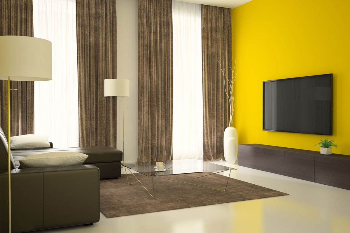 Dark brown Curtains on a yellow wall with a tv mounted in it with a gray sofa
