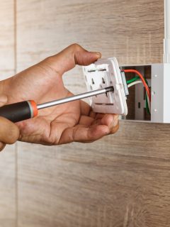Electrician is using a screwdriver to install a power outlet in to a plastic box on a wooden wall - How Much Does It Cost To Move An Electrical Outlet