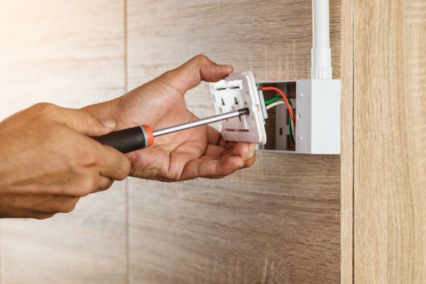 Electrician is using a screwdriver to install a power outlet in to a plastic box on a wooden wall - How Much Does It Cost To Move An Electrical Outlet