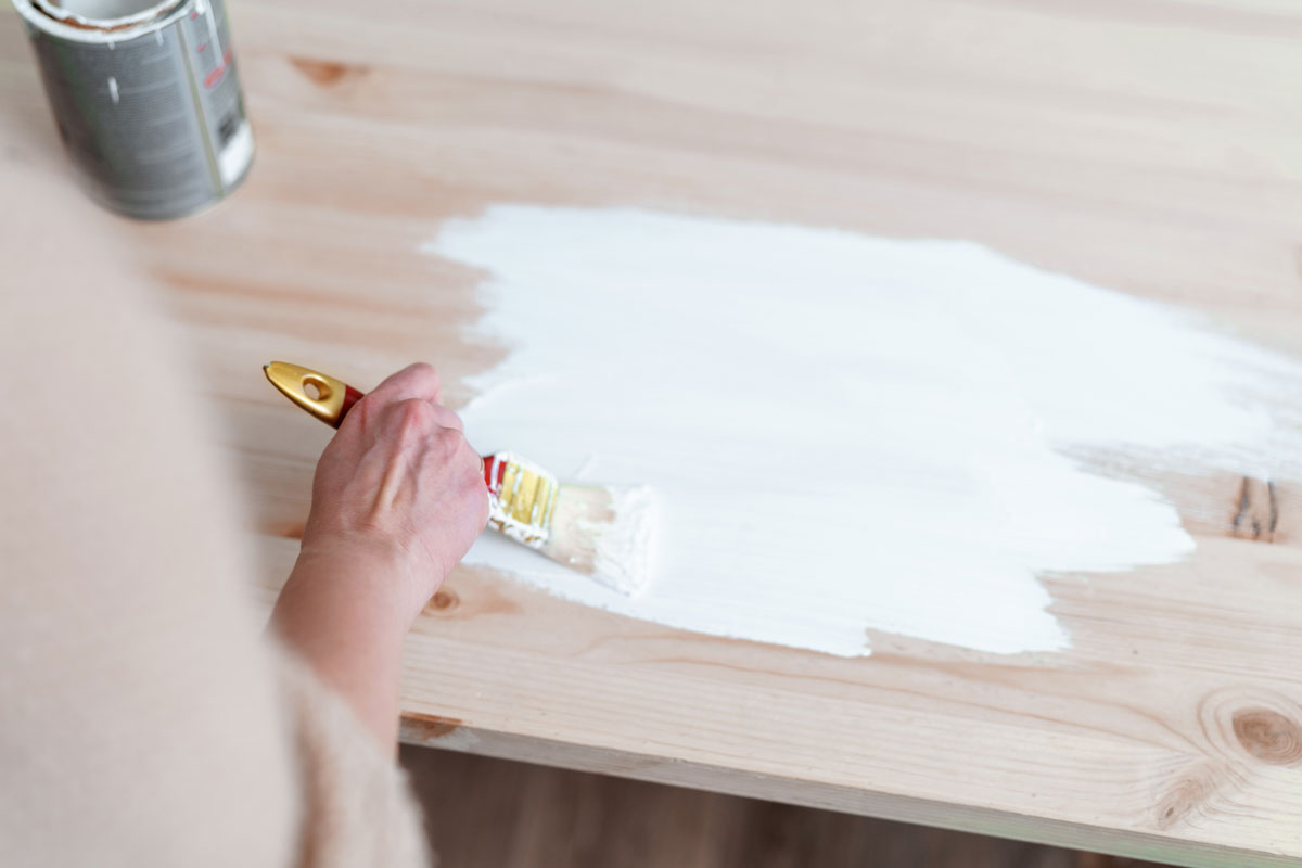 Female hand with a brush to apply white paint on wooden furniture