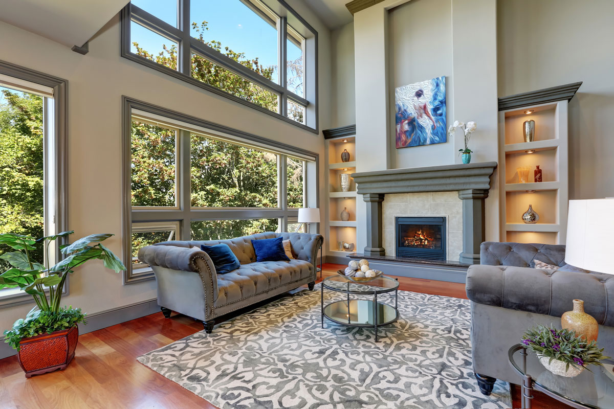 Grey interior of high vaulted ceiling family room in luxury house with fireplace and large windows
