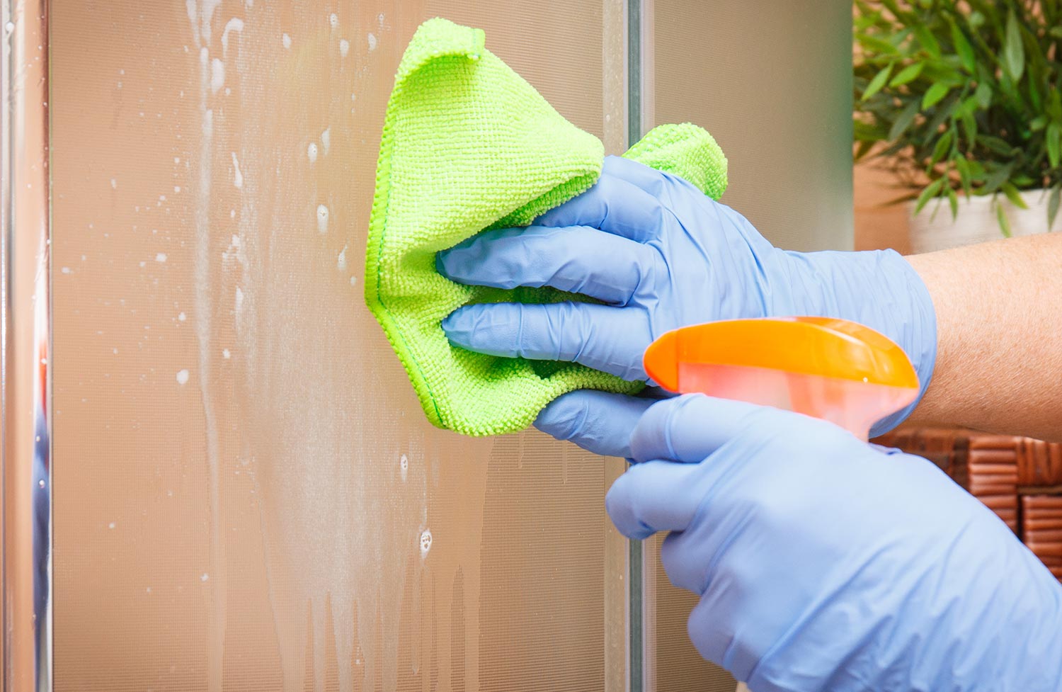 Hand of senior woman in protective gloves cleaning shower using microfiber cloth and detergent