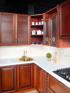 Interior of modern kitchen in classic style with golden elements cherry alder wood cabinetry with built-in appliances electric or induction hob, electric oven stone sink and extractor fan, What Color Hardware For Cherry Cabinets?