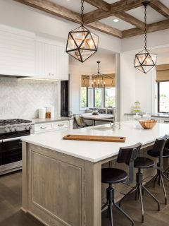 Kitchen Interior with Island, Sink, Cabinets, and Hardwood Floors in New Luxury Home. Features Elegant Pendant Light Fixtures, and Farmhouse Sink next to Window - Where Should A Kitchen Be Located In A House