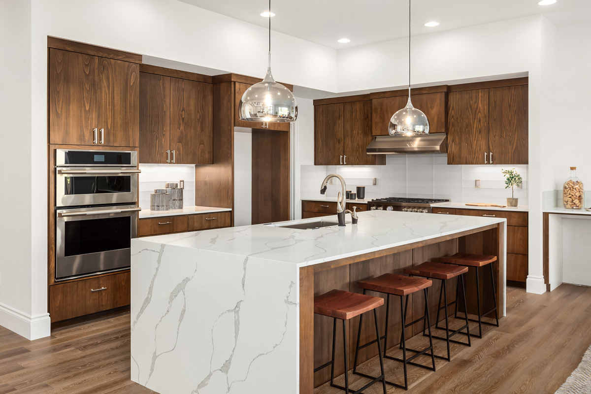 Kitchen in new luxury home with quartz waterfall island, hardwood floors, dark wood cabinets, and stainless steel appliances