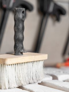 Large brush, which artisan used to clean surface of decorative tiles from dust, stands on desk in foreground, close up, side view, How To Whitewash Tile