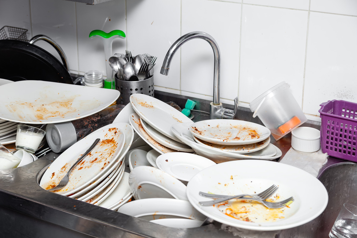 Large metal sink with dirty dishes in professional restaurant kitchen, stack of unclean white plates, tableware, appliances with leftover food, water tap, tiled wall