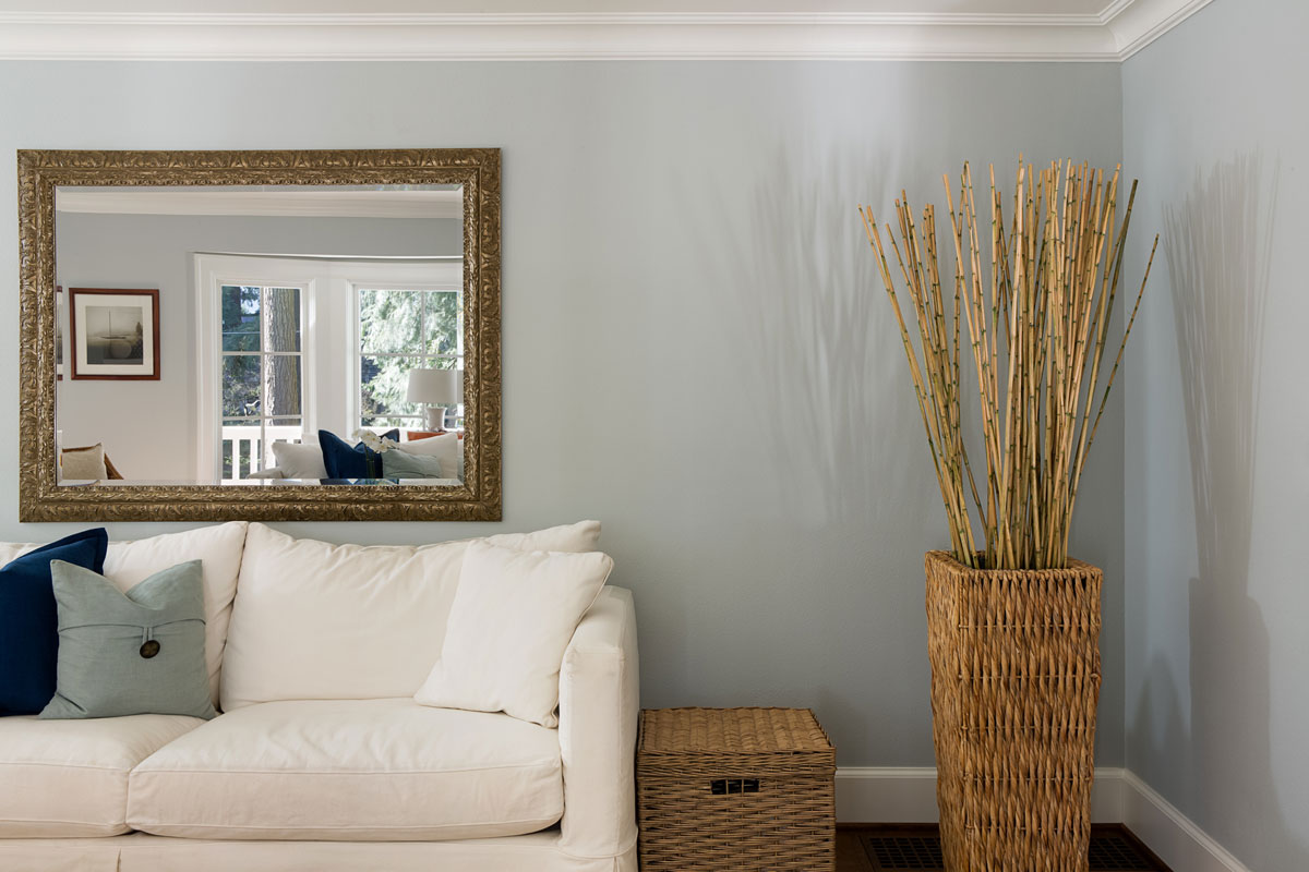 Living room interior with white couch and basket with a bamboo plant and a big mirror on the wall