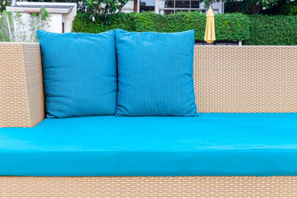Long brown wicker sofa and blue cushions and cushions placed on the lawn