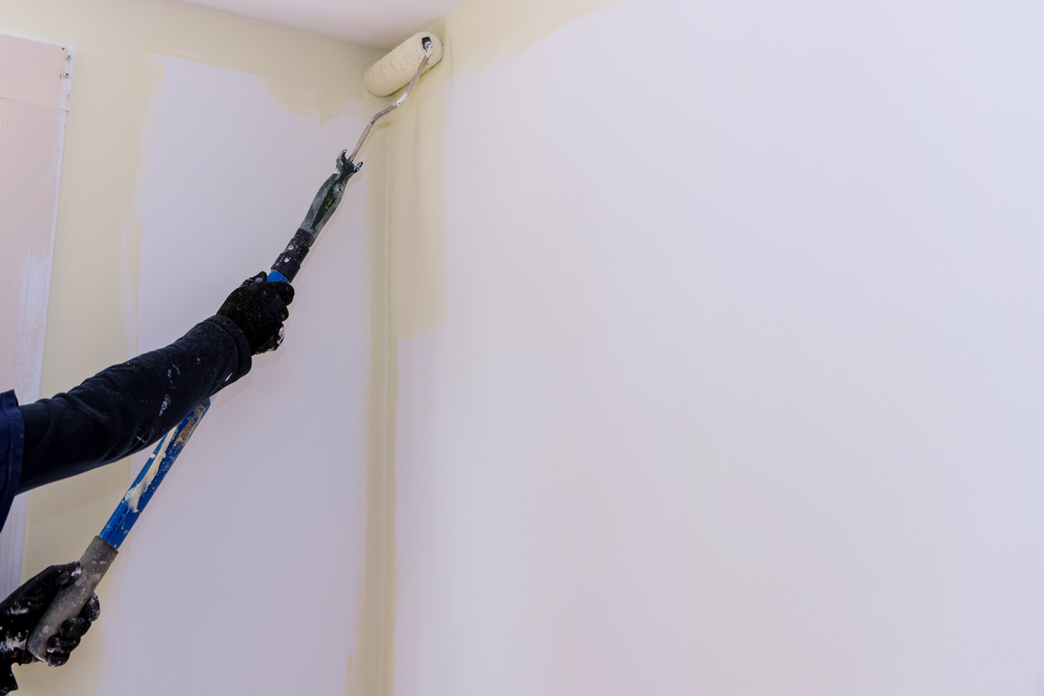 Long handle paint roller brush applying white primer paint on wall with home renovation