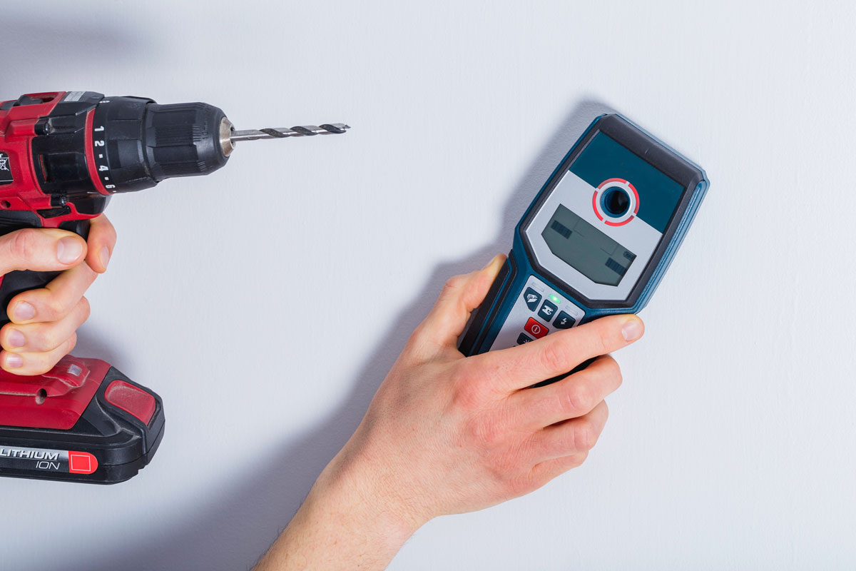 Man hand is scanning wall by cable detector to find a cable before drilling in