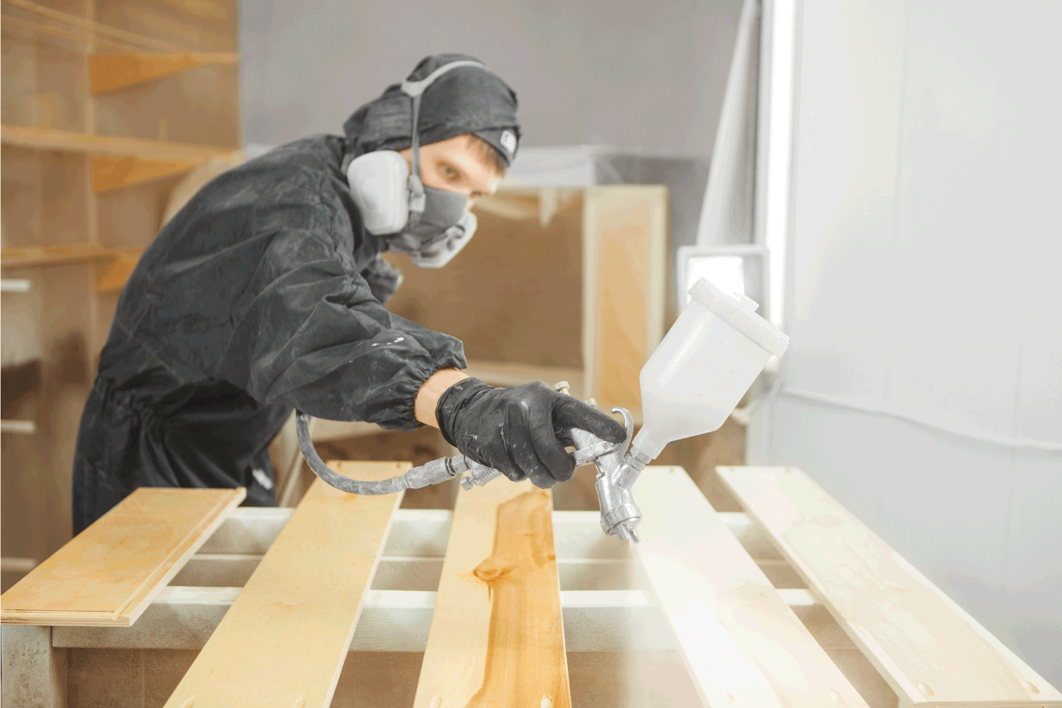 Man in respirator mask painting wooden planks at workshop.