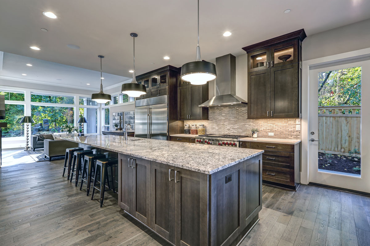 Modern kitchen with brown kitchen cabinets, oversized kitchen island with bar stools and granite countertops