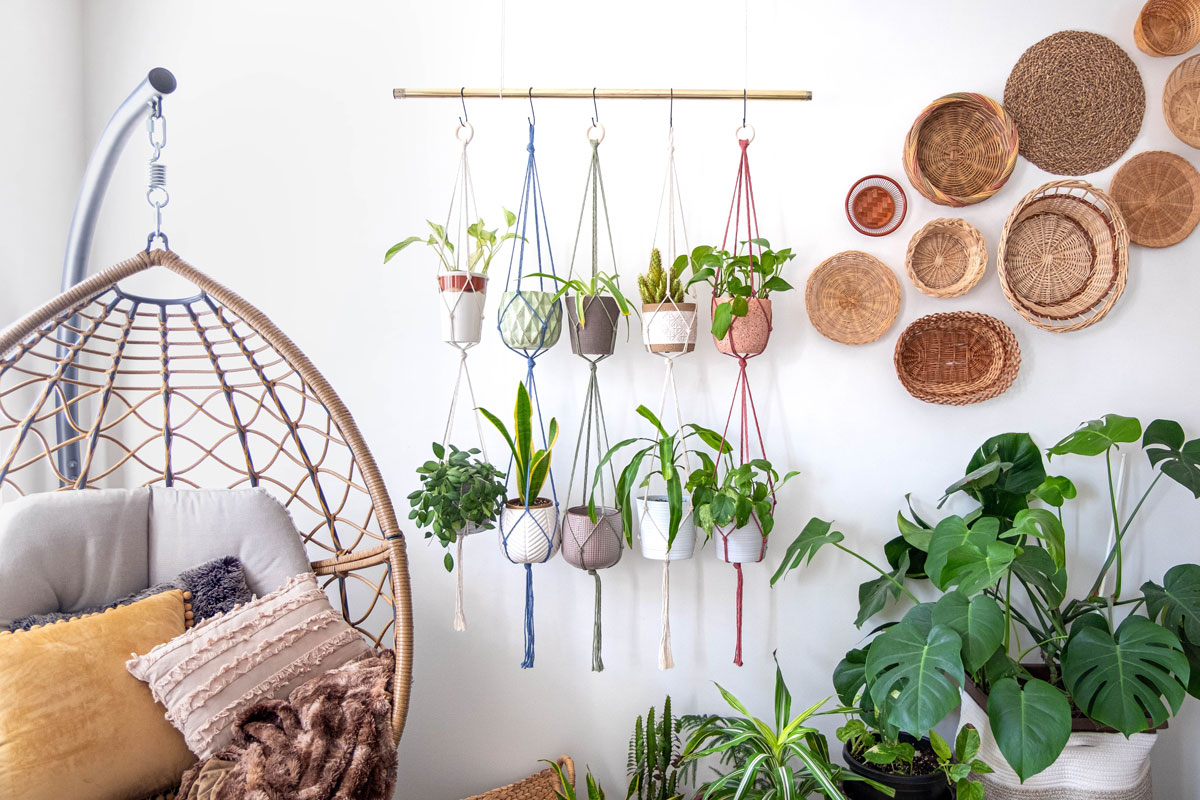 Multiple macrame plant hangers with indoor houseplants and pot planters are hanging from a metal pole. Boho basket wall decor