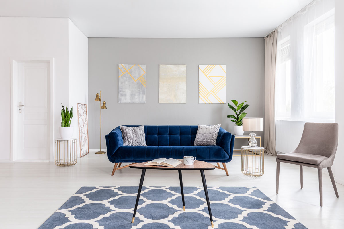 Open space living room interior with modern furniture of a navy blue settee, a beige armchair, a coffee table and other object