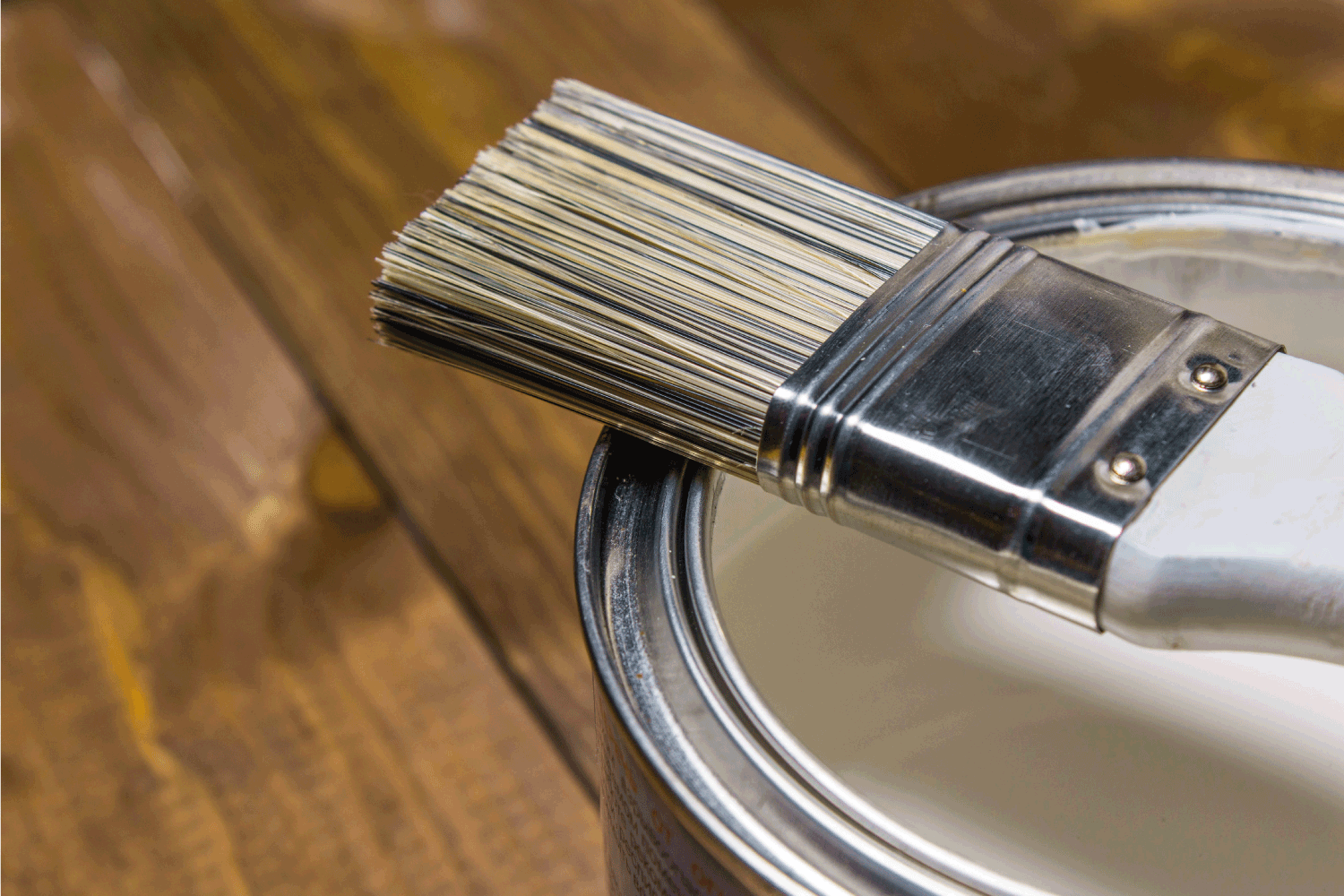 Paint brush on a tin can with white paint close-up, against a background of a wooden texture of a table