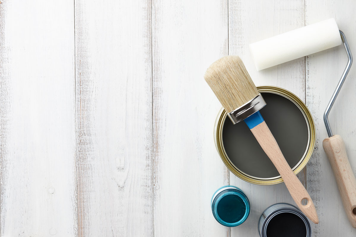 Paint brush, sponge roller, paints, waxes and other painting or decorating supplies on white wooden planks