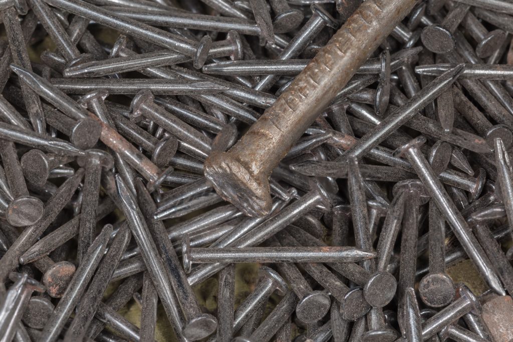Pile of the small thin steel nails and upper part of a big nail on a foreground