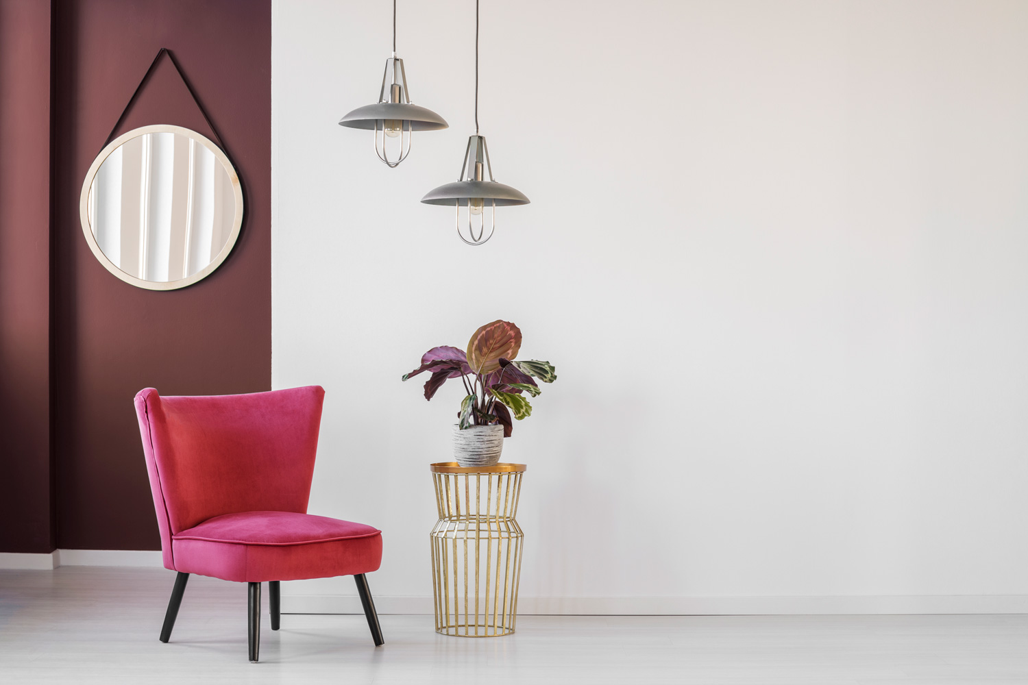 Pink armchair next to a golden, side table with a plant on empty wall in living room interior