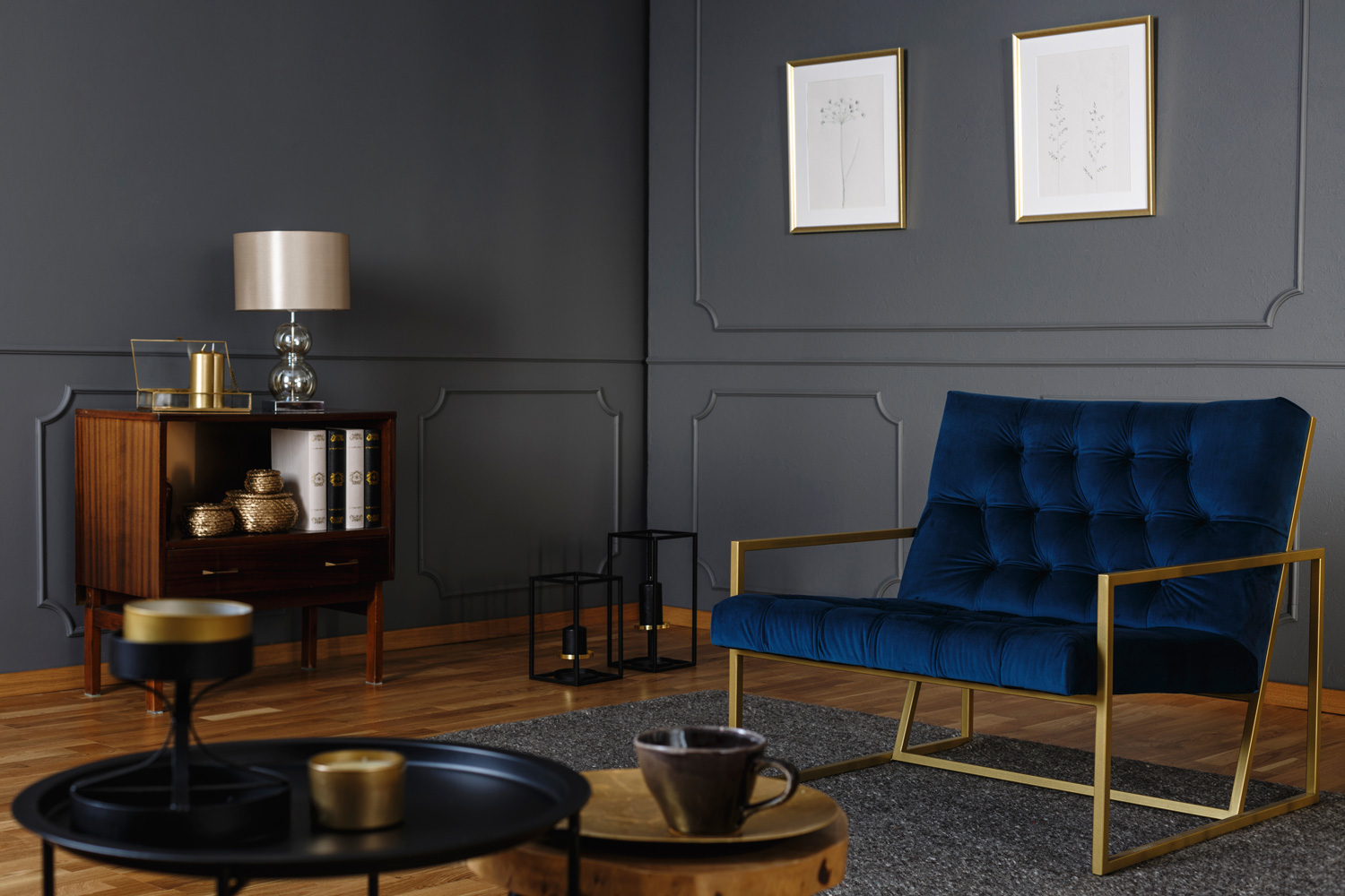 Real photo of a navy blue armchair with a golden frame standing against dark wall with molding in living room interior with gray rug on wooden floor