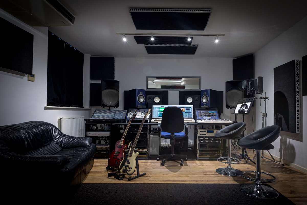 Recording studio control room complete with mixing desk, computer and outboard equipment. Also in the image are guitars, keyboard