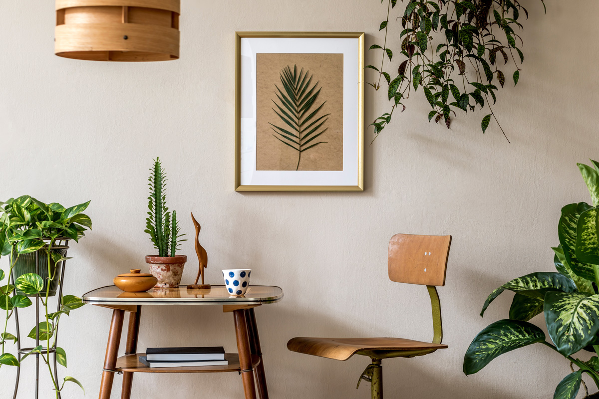 Retro interior design of living room with stylish vintage chair and table, plants, cacti, personal accessories and gold mock up poster frame on the beige wall