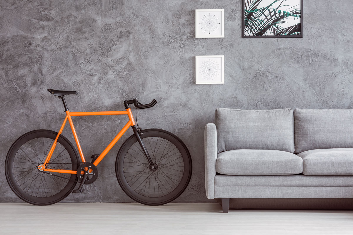 Stylish living room interior with comfy couch, tropical leaf print poster and urban bicycle standing against gray concrete