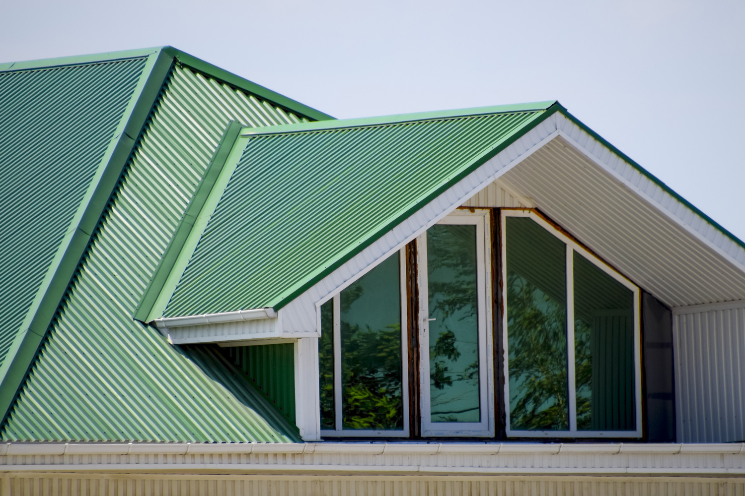 The house with plastic windows and a green roof of corrugated sheet. Roofing of metal profile wavy shape on the house with plastic windows. Green roof of corrugated metal profile and plastic windows.