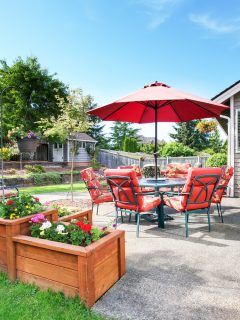 Well kept garden at backyard with concrete floor patio area and opened red umbrella. Northwest, USA - How Thick Should Concrete Be For A Patio
