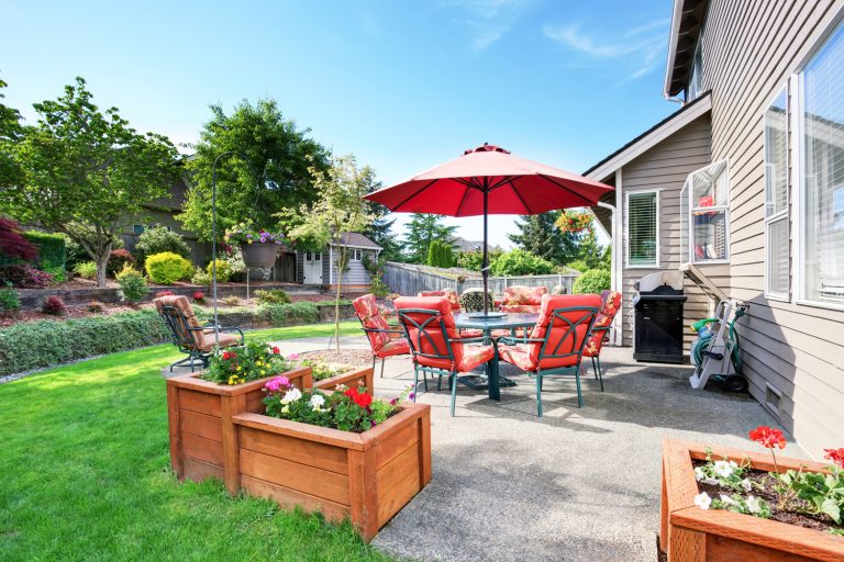Well kept garden at backyard with concrete floor patio area and opened red umbrella. Northwest, USA - How Thick Should Concrete Be For A Patio