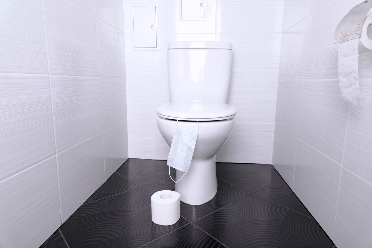 White home toilet with flush and white toilet paper and disposable medical mask in the bathroom