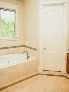 Wooden framed vanity and matching tan countertop and a white bathtub next to a window, 12 Brown Bathroom Floor Tile Ideas