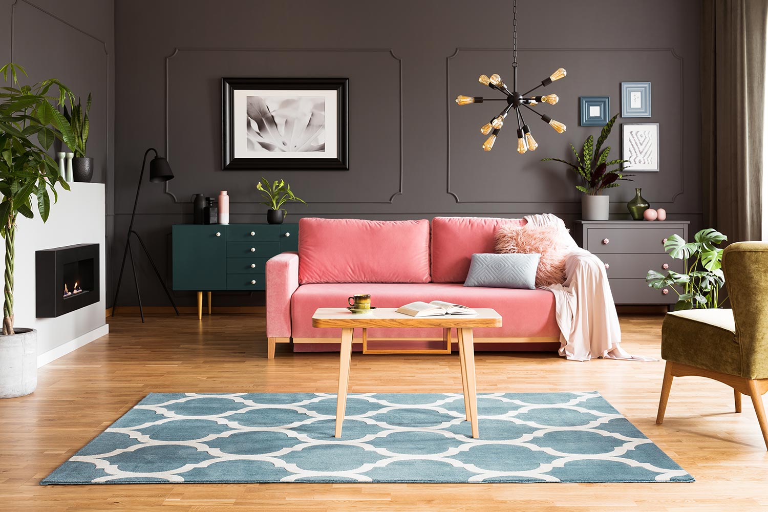 Wooden table on blue carpet in grey living room interior with fireplace and pink sofa
