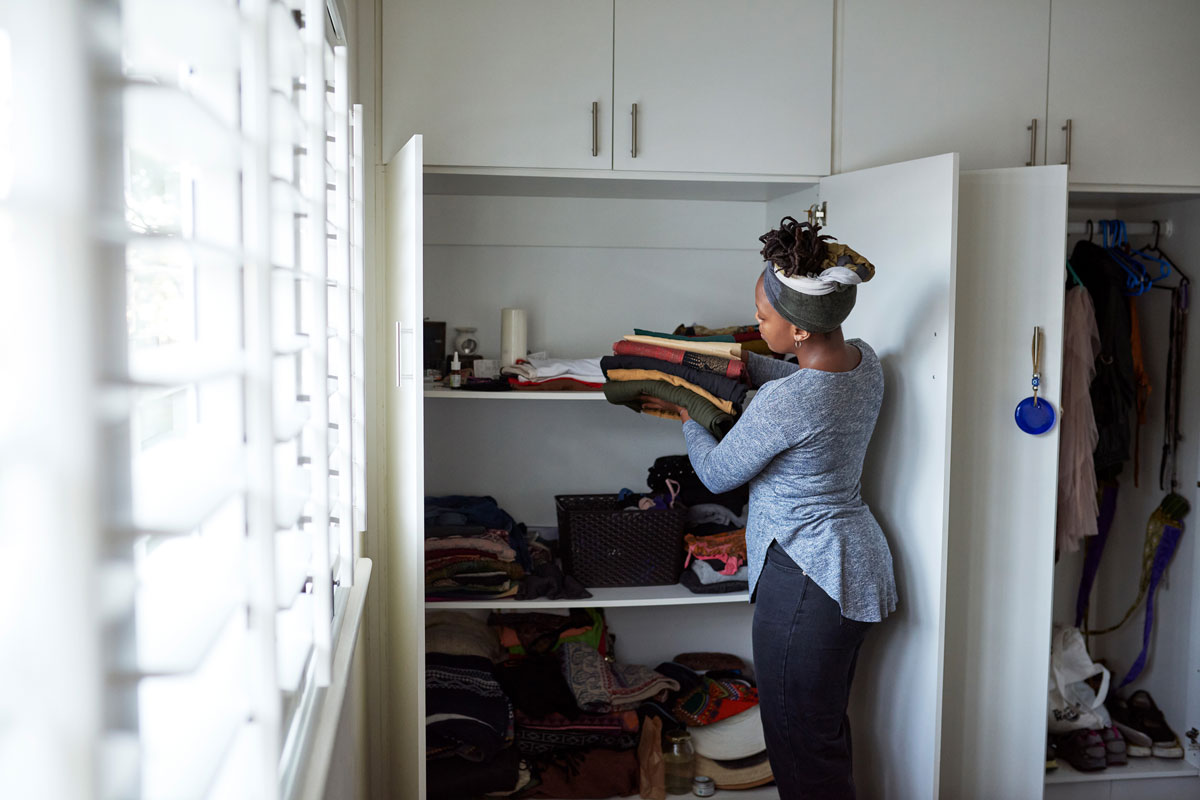 a young woman packing away clean laundry at home then putting folded clothes in closet
