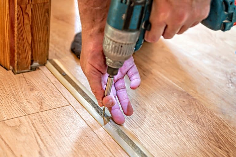 the master screws the thresholds in the doorway on the laminate floor, hands close-up - How To Install Transition Strip In Doorway