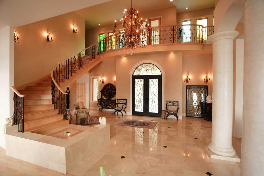 A luxurious marble entryway for a modern and luxurious mansion with huge classic chandeliers and wall lamps on the side