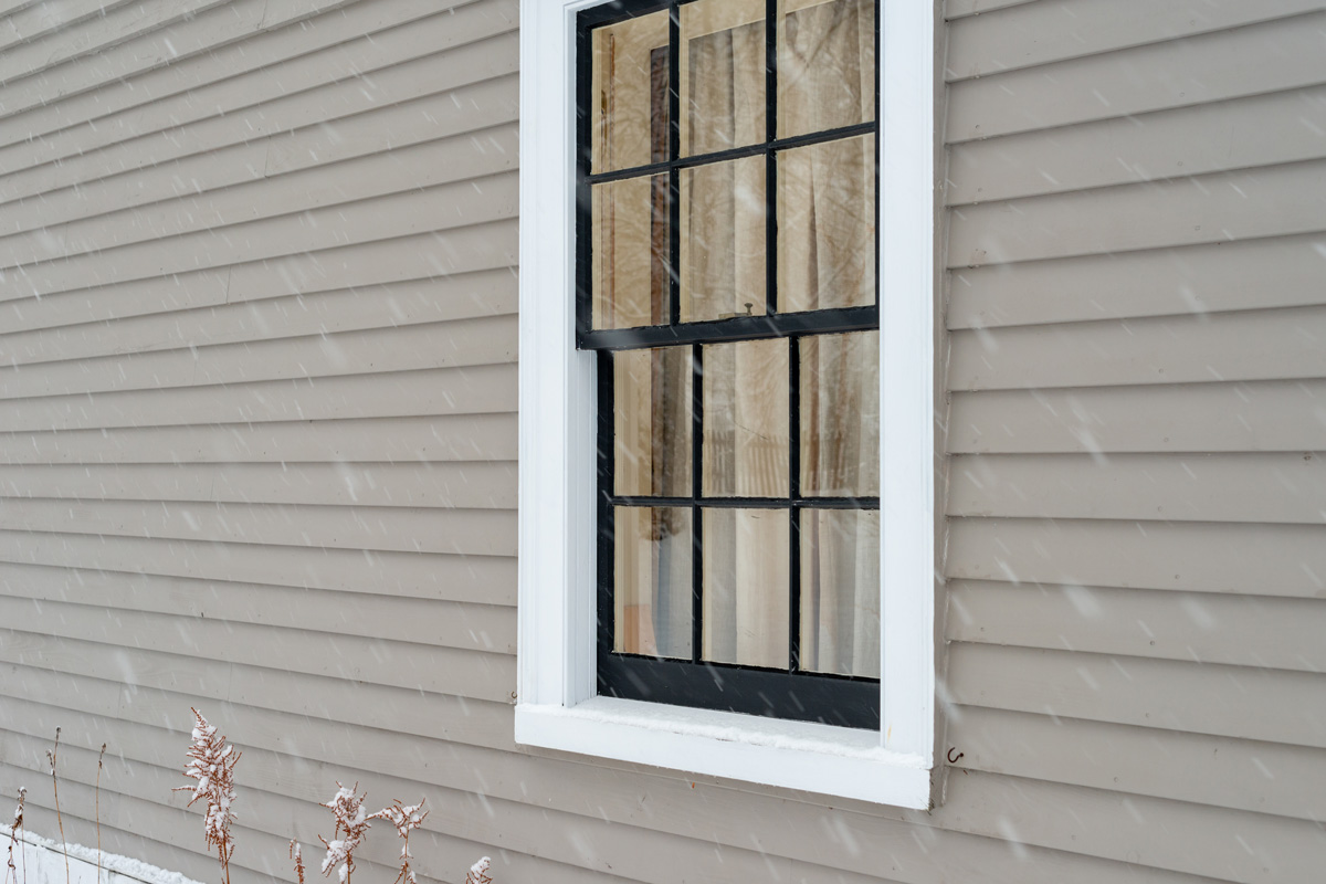 A vintage double hung window with reflecting glass on a beige color exterior wall of a building.