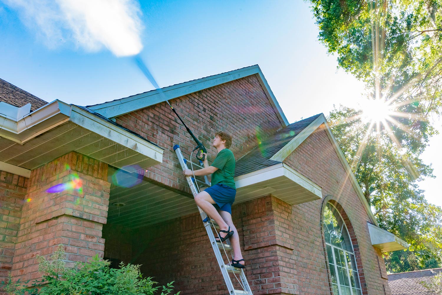 A young man cleans a red brick house exterior
